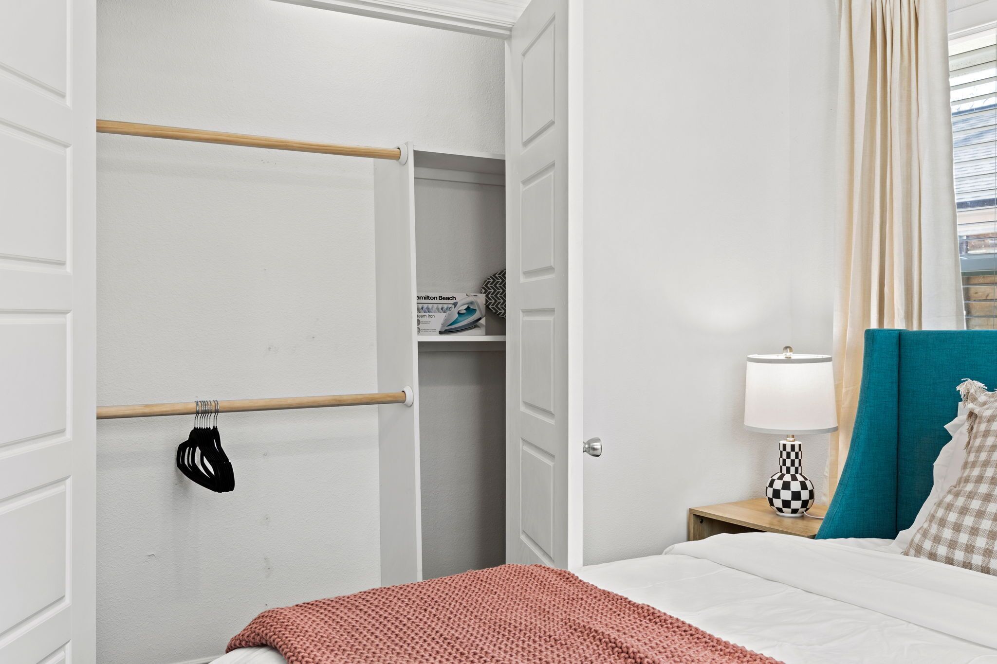 Een hotelkamer met een bed, een nachtkastje met lamp, een kledingkast en een raam met gordijnen.