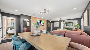 Ein modernes Wohnzimmer mit einem Holzesstisch, blauen Stühlen, einem rosa Sofa und einer Küche im Hintergrund.