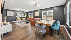 Ein modernes Wohnzimmer mit einem Holzesstisch, blau gepolsterten Sesseln, einem braunen Sofa und einer grauen Akzentwand.