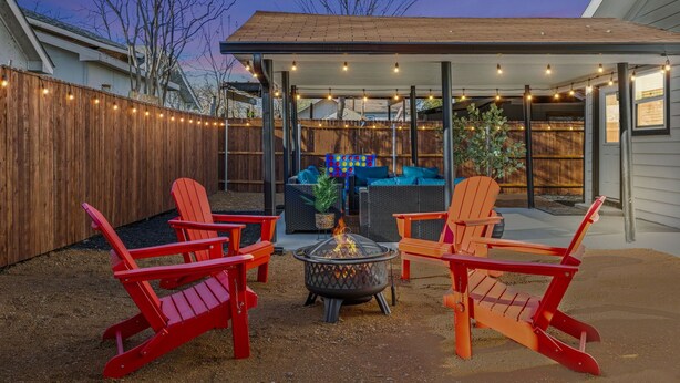 Eine überdachte Terrasse im Freien mit roten Adirondack-Stühlen, einer Feuerstelle und Lichterketten.