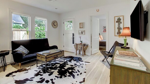A living room with a black sofa, a cowhide rug, a vintage suitcase coffee table, and a TV mounted on the wall.