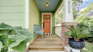 A porch with a wooden bench, a door, and a large potted plant.