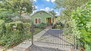A green house with a red door, surrounded by a gravel driveway and a metal gate.