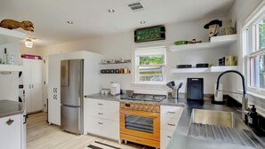 A modern kitchen with a stainless steel refrigerator, an oven, a gas stove, and a sink. There is a window with a view of greenery outside, and a sign above the stove that reads "MYERS PUMPS".