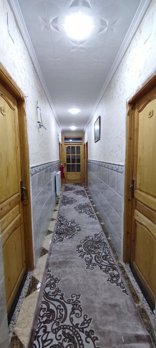 A hallway with patterned carpet, wooden doors, and tiled walls. - mirana mayotte hostel 47 (Ghardaia)