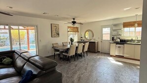 Un salon moderne avec un canapé en cuir, un coin repas avec des chaises, une cuisine avec des meubles blancs et une grande fenêtre.