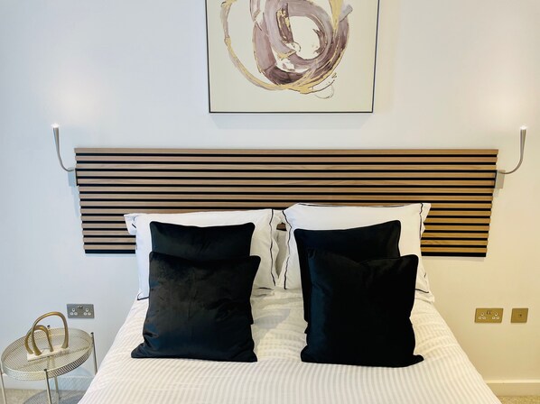A neatly made bed with black and white pillows, a modern headboard, and a small round table with a metal frame. - Spacious 1 Bedroom Apartment in St Albans (St Albans)