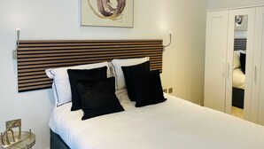 A neatly made bed with a wooden headboard, two black pillows, and a white comforter. - Spacious 1 Bedroom Apartment in St Albans (St Albans)