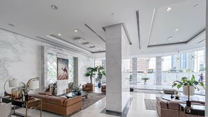 Um hall amplo com design moderno, com área de estar grande com sofás e poltronas, uma coluna central e amplas janelas com vista para a paisagem urbana.