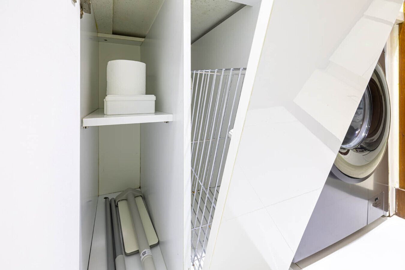 A laundry room with a washing machine, shelves with laundry supplies, and a metal rack.
