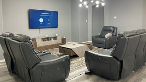 Un soggiorno moderno con una TV a schermo piatto, poltrone in pelle, un tavolino da caffè e un originale lampadario.