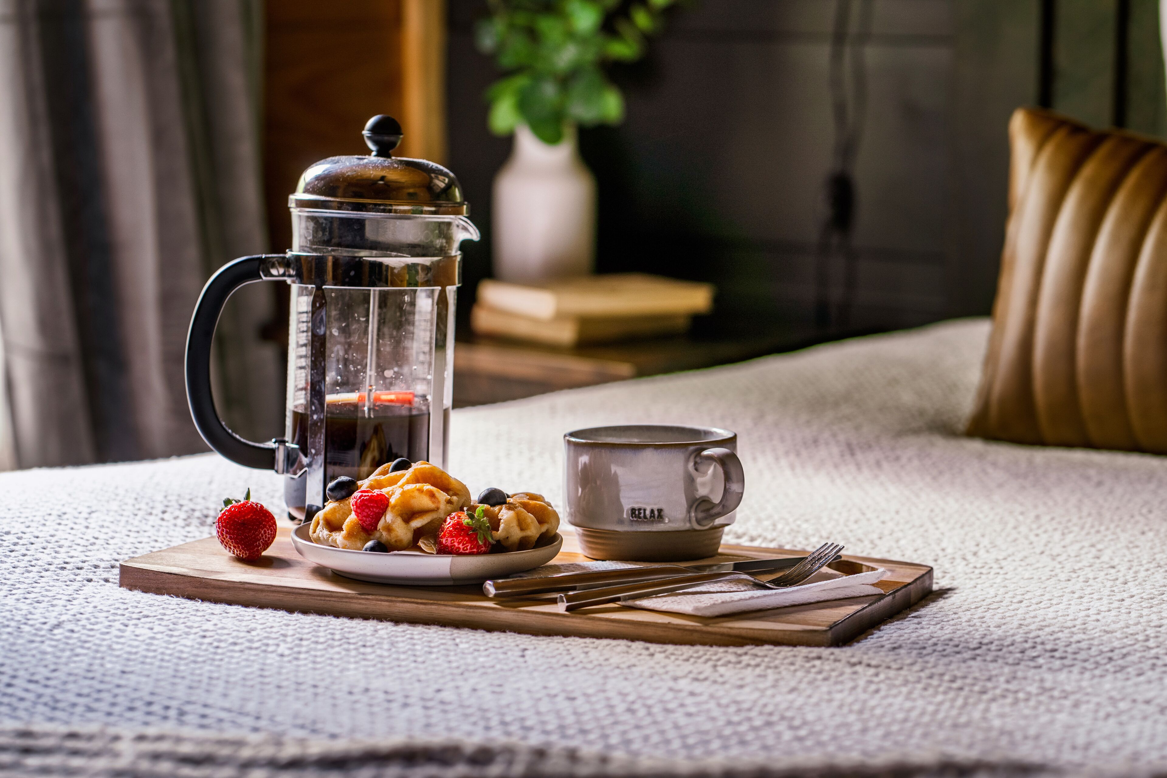 A coffee maker, a cup, and a plate with waffles and berries on a wooden board.