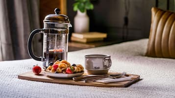 A coffee maker, a cup, and a plate with waffles and berries on a wooden board.