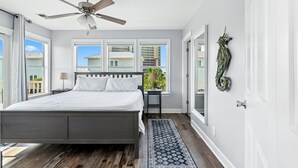 Un dormitorio con cama, ventilador de techo, ventanas y vistas a edificios.