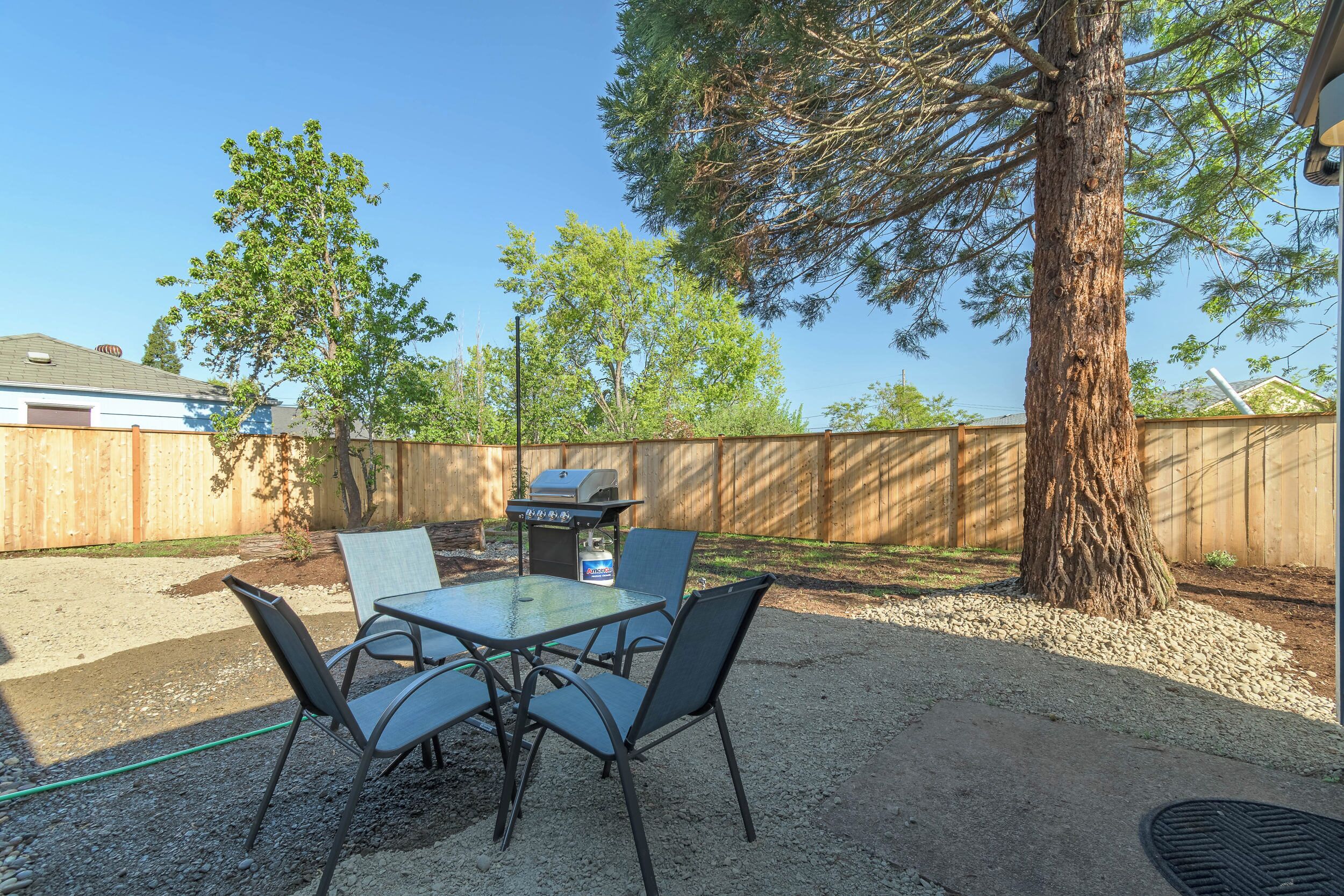 Une terrasse extérieure avec une table et des chaises, un barbecue et un arbre.