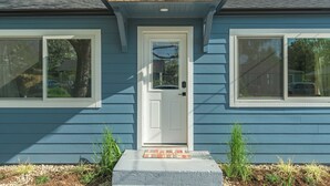 Une maison bleue avec une porte blanche, deux fenêtres et un petit porche agrémenté de plantes.