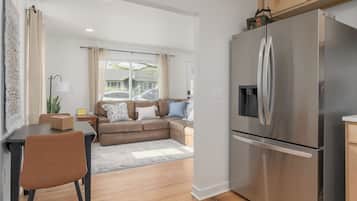 Een moderne keuken met een koelkast van roestvrij staal, houten keukenkastjes en een eethoek met een tafel en stoelen.