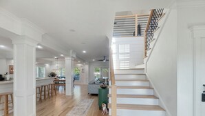 A spacious living area with a wooden staircase, a kitchen, and a dining area. - Farmhouse Near the Shore - 3 King Suites, Hot Tub, 10 Minutes to Beach (Supply)
