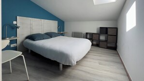 A bedroom with a bed, a desk, a chair, a radiator, and built-in shelving. - Furnished apartment with swimming pool (Saint-Georges-d'Oléron)