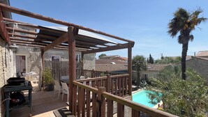 A wooden deck with a pool, stone walls, and a palm tree. - Furnished apartment with swimming pool (Saint-Georges-d'Oléron)
