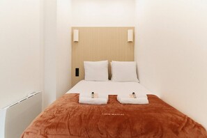 A hotel room with a bed, two pillows, a headboard, and a brown blanket.