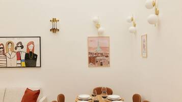 A dining area with a wooden table set for four, surrounded by brown chairs. There are wall-mounted light fixtures and framed artwork on the walls.