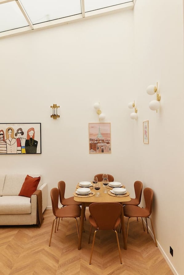Ein Essbereich mit einem Holztisch, gedeckt für vier Personen, umgeben von braunen Stühlen. An den Wänden befinden sich wandmontierte Leuchten und gerahmte Kunstwerke.