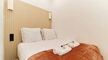 A hotel room with a bed, pillows, a headboard, a wall-mounted light, and a neatly folded towel on the bed.