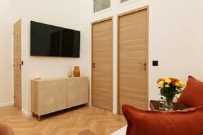 Ein modernes Zimmer mit Flachbildfernseher an der Wand, einem Holzschrank mit Vase und Kerzen sowie einem Tisch mit Blumenvase.