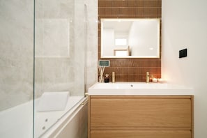 Une salle de bain moderne avec une douche à l’italienne en verre, une baignoire blanche et un meuble-lavabo en bois surmonté d’un grand miroir.