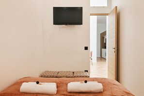 Ein Hotelzimmer mit einem Bett, zwei Handtüchern, einem an der Wand befestigten Fernseher und einer Tür zu einer Küchenzeile.