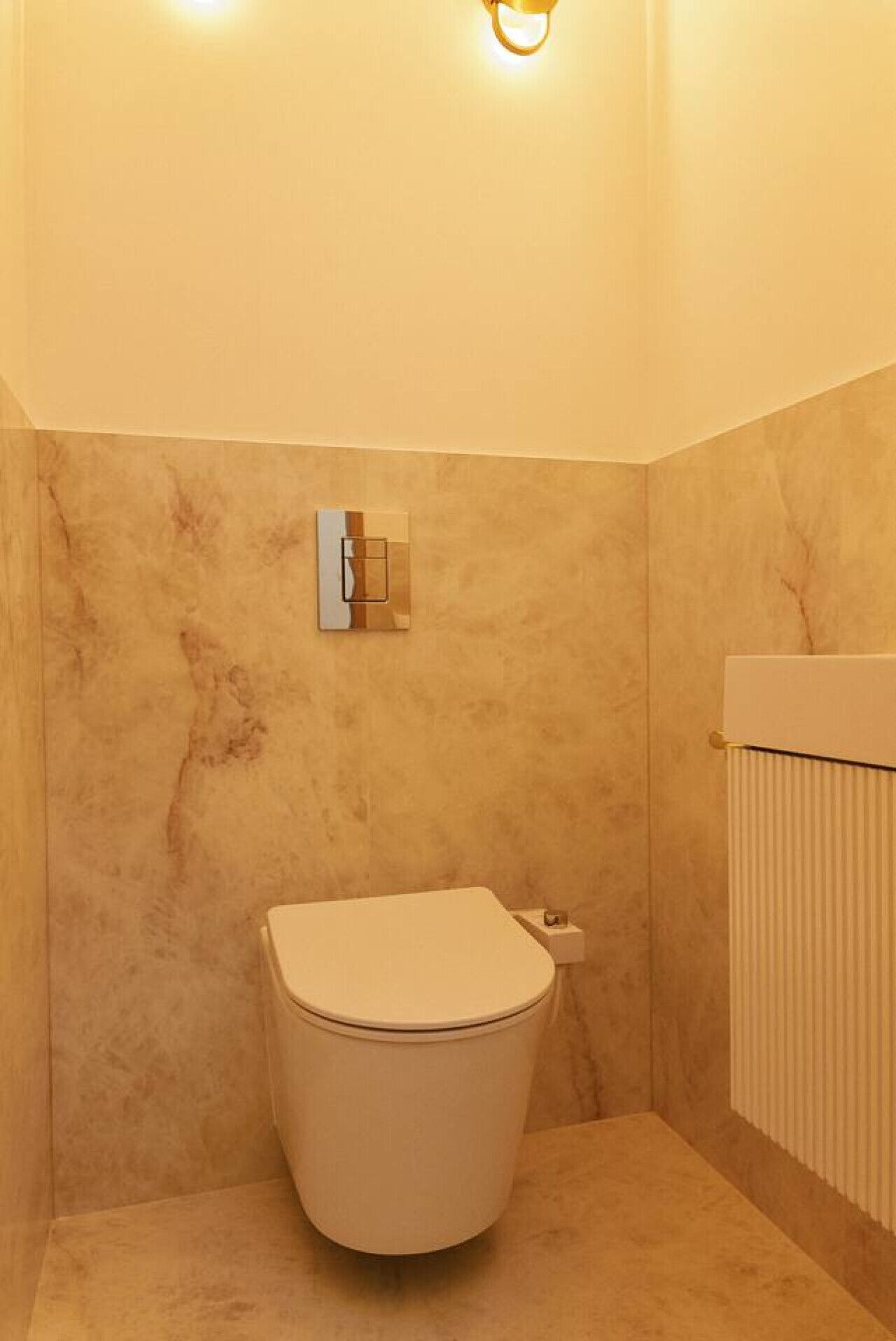 A compact bathroom with a toilet, a wall-mounted light fixture, and a radiator.