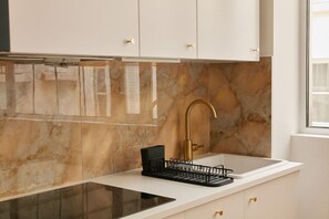 Cocina moderna con armarios blancos, encimera negra, grifo dorado y escurreplatos negro.