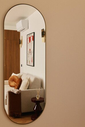 Una sala de estar con un sofá, una mesita auxiliar y un espejo que refleja la habitación.