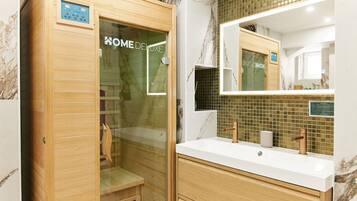 A modern bathroom with a wooden cabinet, a glass shower enclosure, and a marble-tiled wall.