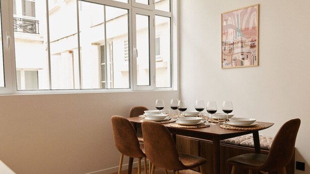 Un comedor con una mesa preparada para seis personas, seis copas de vino y un cuadro de un paisaje urbano en la pared.