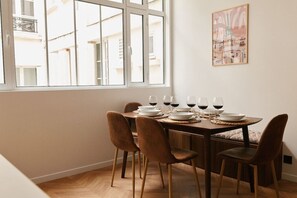 Un coin repas avec une table dressée pour six personnes, six verres à vin et un tableau représentant un paysage urbain accroché au mur.