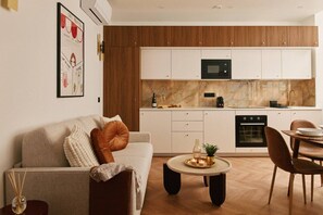 A modern kitchen with white cabinets, a microwave, and an oven. There is a dining area with a table and chairs. - Lavie Maison Chic Sauna Hot Tub (Paris)
