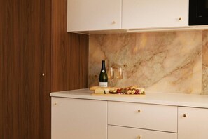 Una cocina con salpicadero de mármol, armarios de madera y una encimera con una botella de vino, copas y una tabla de embutidos.