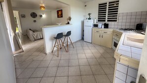 A compact kitchen with a dining area, a refrigerator, a microwave, a stove, and a sink. - Villa apartment with private garden – quiet – 4 guests – Sainte-Anne (Sainte-Anne)