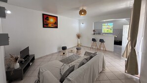 A modern living room with a sofa, a TV, a painting, and a kitchen area in the background. - Villa apartment with private garden – quiet – 4 guests – Sainte-Anne (Sainte-Anne)