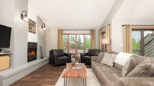 Una sala de estar moderna con chimenea, sillones de cuero, una mesa de centro de madera y un ventanal con cortinas.