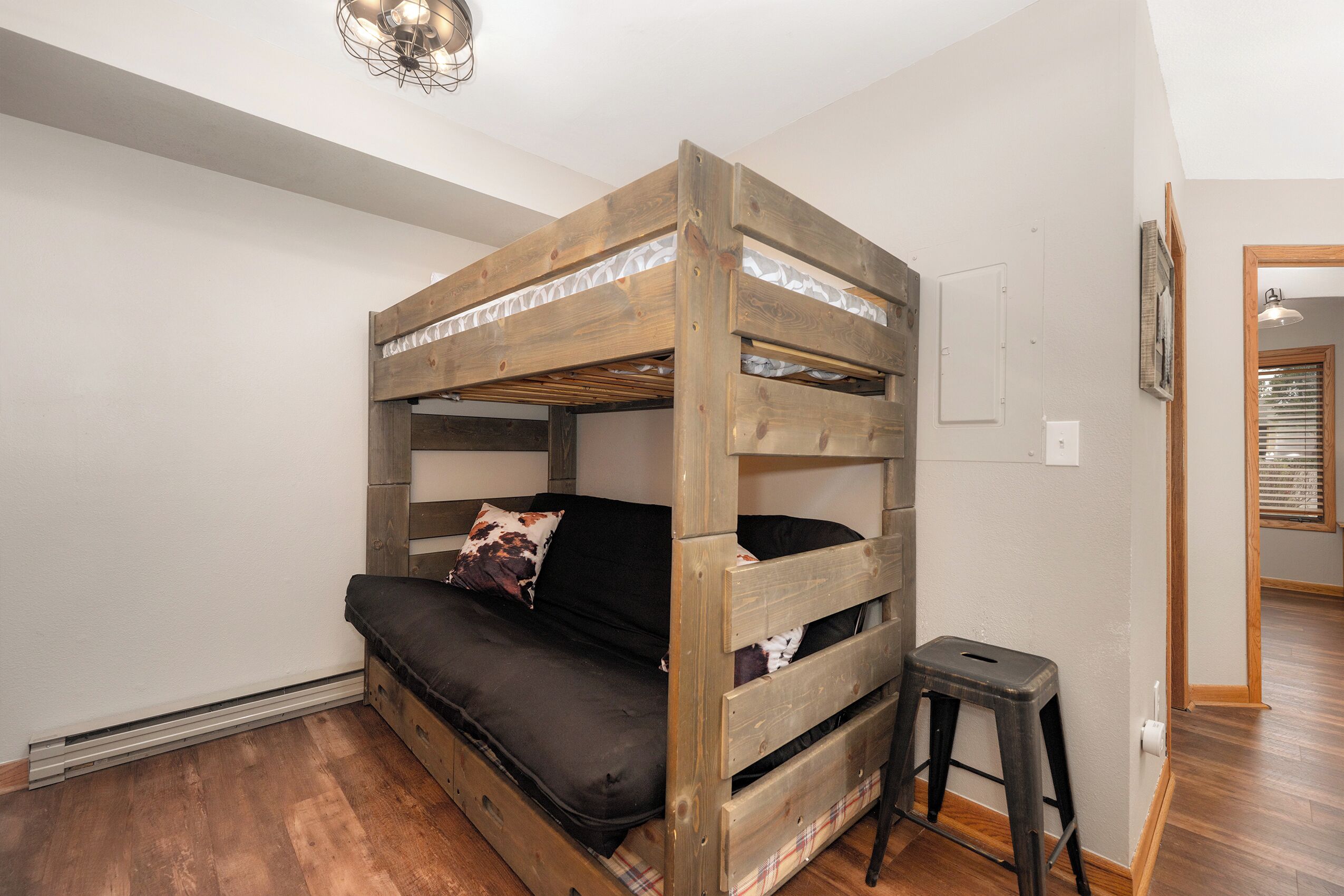Un lit superposé avec un matelas et des oreillers, un petit tabouret et un luminaire au plafond.