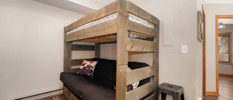 Un lit superposé avec un matelas et des oreillers, un petit tabouret et un luminaire au plafond.