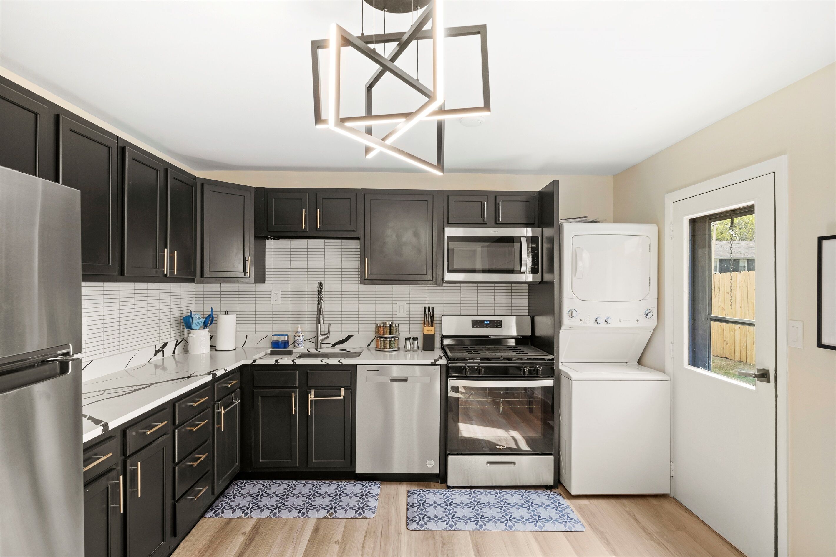 A modern kitchen with dark cabinets, stainless steel appliances, and a unique geometric light fixture.