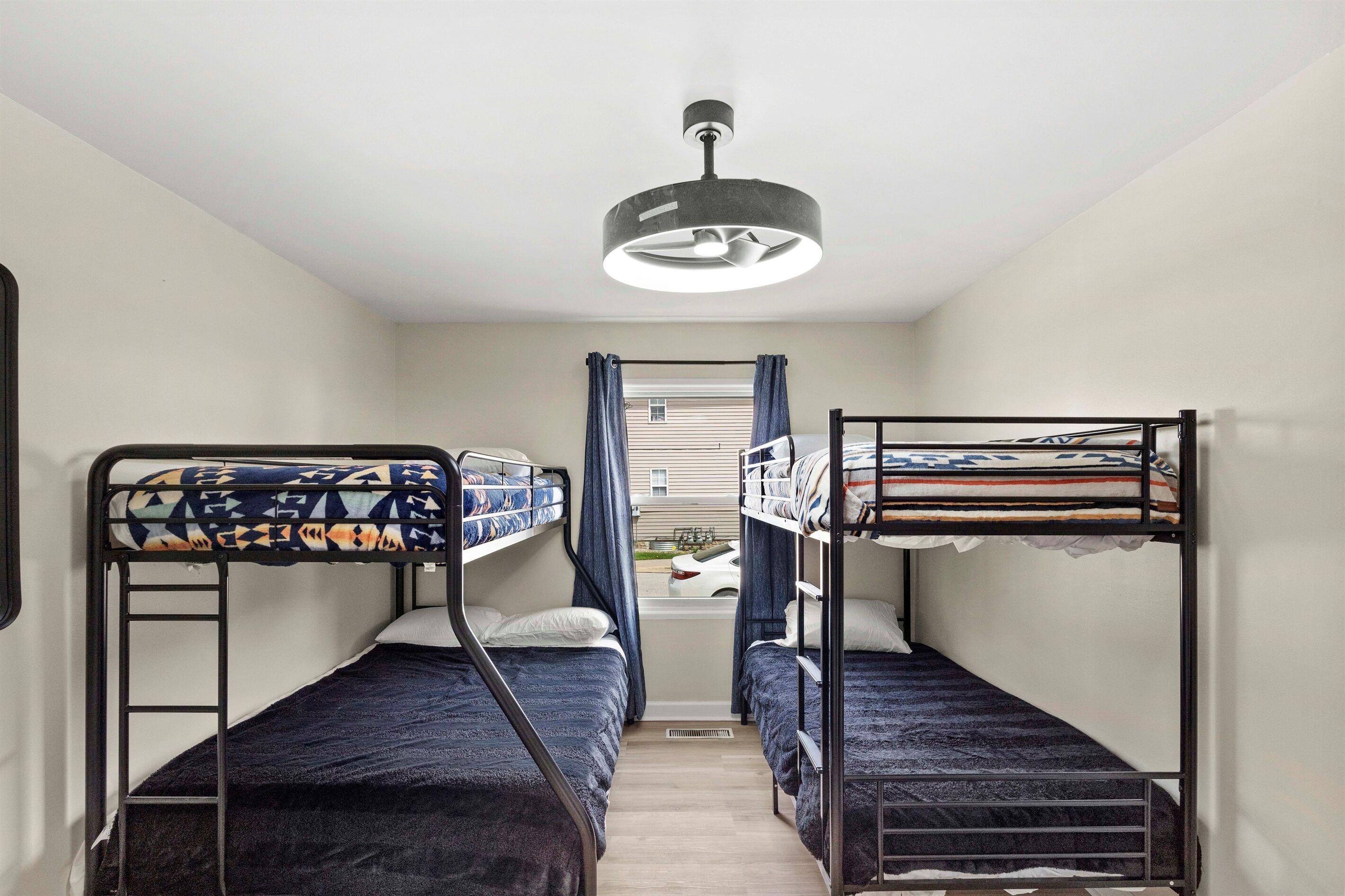 A compact room with two bunk beds, a ceiling fan, and a window with curtains.