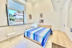 Une chambre à coucher comprenant un lit, une chaise, un bureau et une fenêtre donnant sur un bâtiment situé à l’extérieur.
