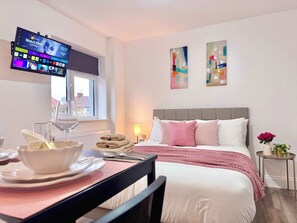 Ein Hotelzimmer mit Bett, einem an der Wand montierten Fernseher, einem Fenster und einem Tisch mit Schüssel und Tellern.