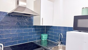 A kitchen with a black stove, stainless steel sink, white cabinets, and blue-tiled backsplash. - Comfy Studio 30min to Central London (Wembley)