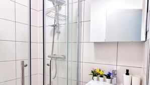 A modern bathroom with a glass-enclosed shower, a white sink, and a mirror above it. - Comfy Studio 30min to Central London (Wembley)